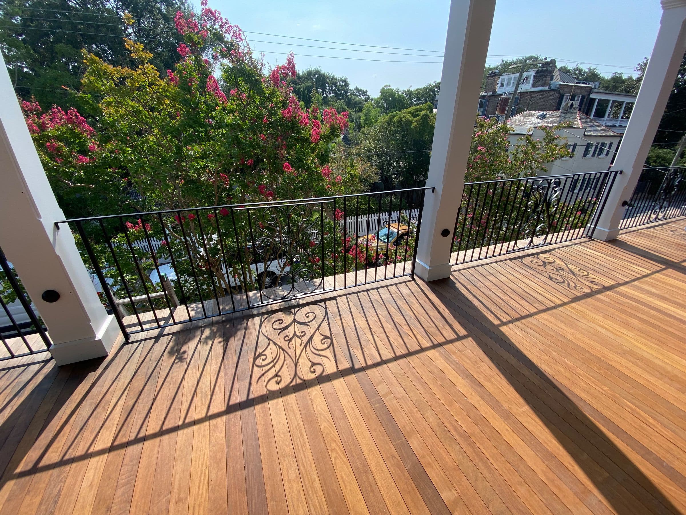 Ipe porch floor with an iron railing and crepe myrtles beyond