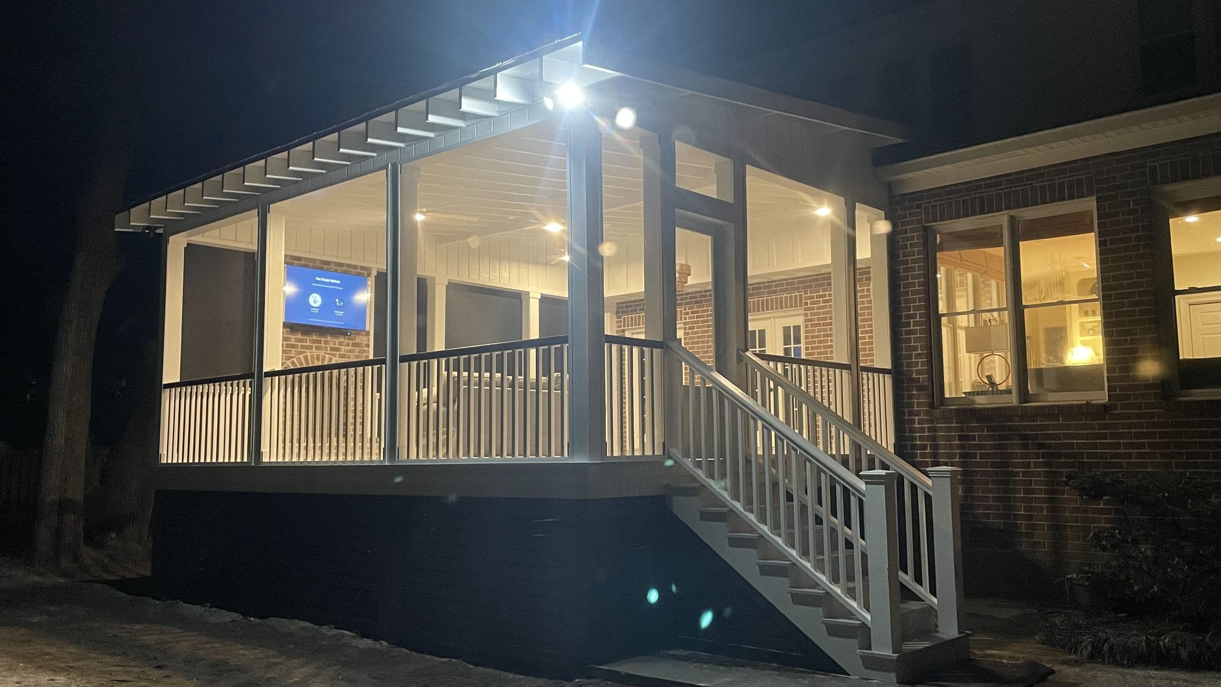 Screened porch addition lit up at dusk, with white rails and a stair down to the yard